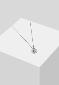 Silvrig halsband med en rund hänge som har en ankh-symbol. Fint kedja med en jämn textur, placerad mot en neutral bakgrund.