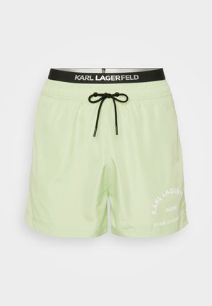 Lys grønne badetights med sort snøre og elastisk talje. Har hvid trykt tekst på nederste venstre side. Glat tekstur.