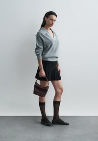 Grijze wollen v-halstrui, zwarte klokrok, doorzichtige zwarte kniehoge sokken, zwarte ballerina's en een kleine bordeauxrode handtas met een gouden accent.