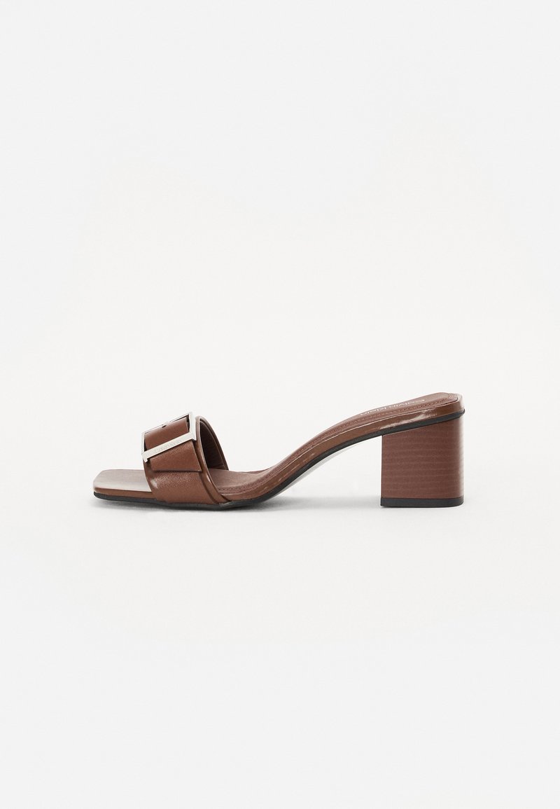 Sandale à talon bloc en cuir marron avec une large sangle ornée d'un accent en argent, bout carré et semelle texturée.