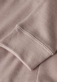 Gros plan sur une manche de sweat-shirt pliée en rose dusty, montrant des coutures détaillées et une texture de tissu doux et tricoté.