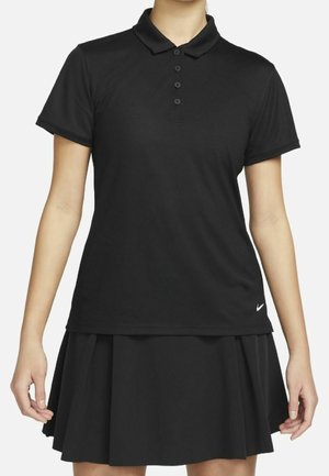 Woman wearing a black short-sleeve polo shirt and a black pleated skirt with a small white Nike logo on the shirt hem.
