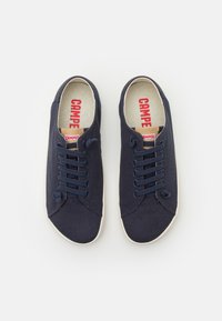 Navy Canvas-Sneakers mit runder Zehenpartie, weißer Gummisohle und blauen Schnürsenkeln. Rotes "Camper"-Logo auf beiger Innensohle.