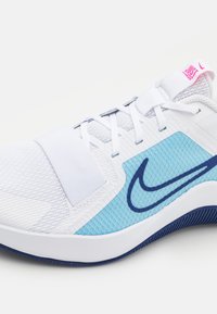 Baskets blanches avec des accents en maille bleue, surfaces texturées et un logo rose. Présente une sangle sur les lacets pour un soutien supplémentaire.