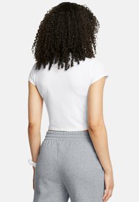Witte korte crop top met korte mouwen, gecombineerd met grijze sweatpants. Zachte stoftextuur, eenvoudig ontwerp, geen zichtbare patronen of accenten.