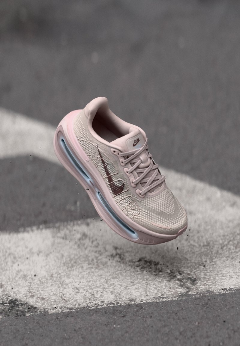 Light pink running shoe with a mesh upper, accented by a darker pink swoosh, featuring a visible air unit in the heel and textured sole.