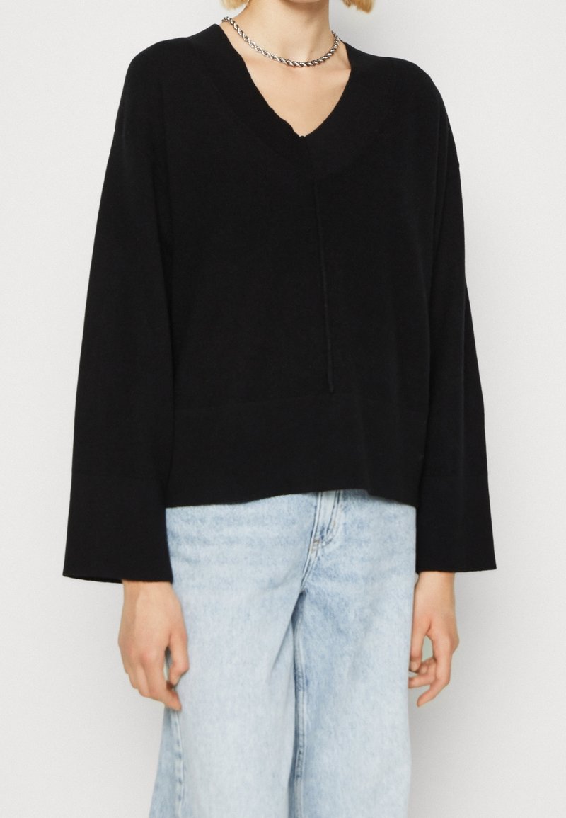 Svart, överdimensionerad V-ringad tröja med långa, vida ärmar. Gjord av mjukt material med ribbat halslinning. Buren tillsammans med ljusblå jeans.