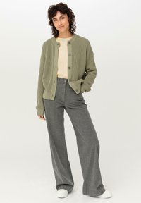 Ljusgrön stickad cardigan med rund halsringning, knappfront och ribbade manschetter, tillsammans med grå vida byxor och vita sneakers.