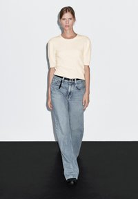 Top in maglia giallo chiaro con maniche corte a sbuffo; abbinato a jeans dritti a vita alta, in denim blu sbiadito; cintura nera. Design semplice e pulito.