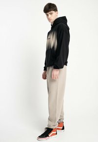 Czarna bluza z kapturem z efektem gradientu, szare dresowe spodnie i czarne sneakersy z pomarańczowymi akcentami. Swobodny krój, miękki materiał i minimalistyczny design.