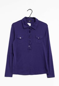 Långärmad lila polo skjorta med krage, fem knappar fram, och två knäppta bröstfickor, hängande på svart galge.