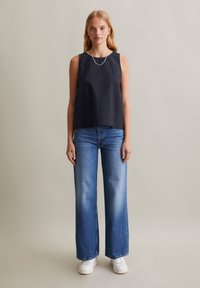 Marineblauw mouwloos shirt in een gestructureerde stof, gecombineerd met lichtblauwe wijde jeans en witte sneakers. Eenvoudig, casual ontwerp met minimale details.