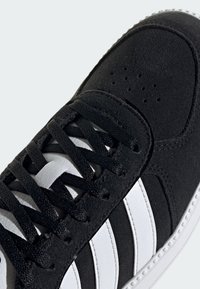 Zapatillas deportivas de ante negro con detalles en cuero blanco, superficie texturizada y cierre clásico de cordones con perforaciones para ventilación.
