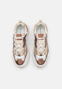 Sneaker chunky che presentano un mix di materiali bianchi, beige e bronzo metallico. Accenti in rete e pelle con texture e forme a contrasto.