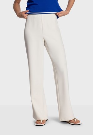 Pantalon blanc léger avec taille élastique et coupe droite. Porté avec un haut bleu et des tongs ; texture lisse et coupe ajustée.