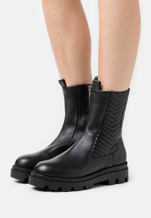 Botas de cuero negro hasta el tobillo con cremallera lateral, panel de chevrón texturizado y suela robusta con profundas pisadas para tracción.