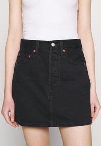 Falda de mezclilla negra con forma ajustada, diseño de cinco bolsillos, herrajes en tono cobre y cierre frontal con botones. Textura suave y longitud por encima de la rodilla.