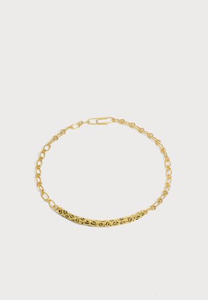 Collier chaîne ton or avec un détail de barre courbée texturée et une fermeture ovale allongée sur un fond clair uni.