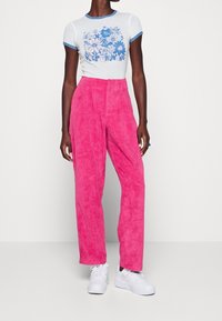 Camiseta blanca con gráfico floral azul y texto, combinada con pantalones de corduroy de talle alto en rosa brillante y zapatillas blancas.