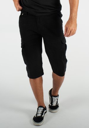 Shorts cargo noirs en coton, avec une coupe mi-genoux, des poches latérales et une coupe décontractée. Associés à des baskets noires et blanches.