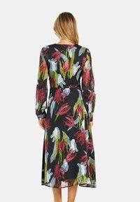 Vestido negro de manga larga con un estampado de flores rojas y azules; material transparente, corte fluido y detalle de cintura ceñida.