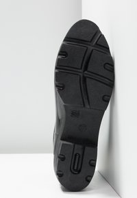 Suola di scarpa in gomma nera con un motivo di battistrada testurizzato, caratterizzata da scanalature e segni. La taglia "37" è impressa vicino al tallone.