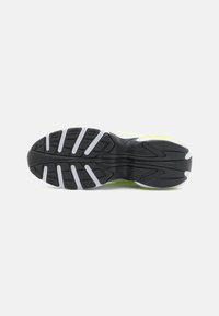 Black athletic shoe sole with gray and white traction patterns, featuring a textured surface and bright yellow accents along the edges.