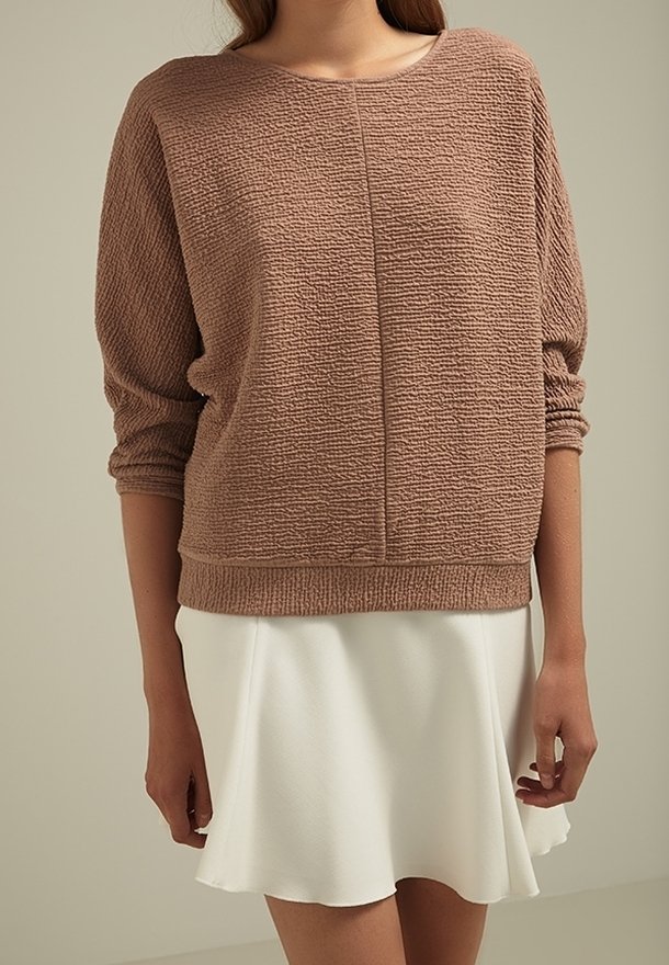 Pulover marrón texturizado con mangas largas y cuello redondo, combinado con una falda blanca de corte acampanado. Tejido suave con un ajuste holgado.