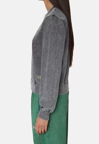 Gray sweatshirt with a crew neck, ribbed cuffs, and hem. Features a small logo detail at the bottom and a smooth fabric texture.