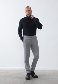 Pull encolure roulée côtelé marine, pantalon à motifs pied-de-poule gris, et bottes noires à lacets. Design ajusté avec des éléments texturés et à motifs.