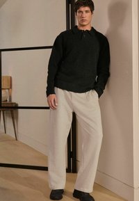 Sort sweater med krave, parret med lysegrå sweatpants og sorte sko. Stoffet ser blødt ud med en afslappet pasform.