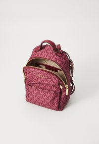 Zaino in tessuto bordeaux con motivo logo MK, scomparti con doppia zip e hardware dorato. Presenta spallacci regolabili e maniglia superiore.