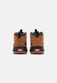 Baskets montantes en suède marron et cuir noir avec semelles en caoutchouc, présentant une languette et le logo Vans au talon.