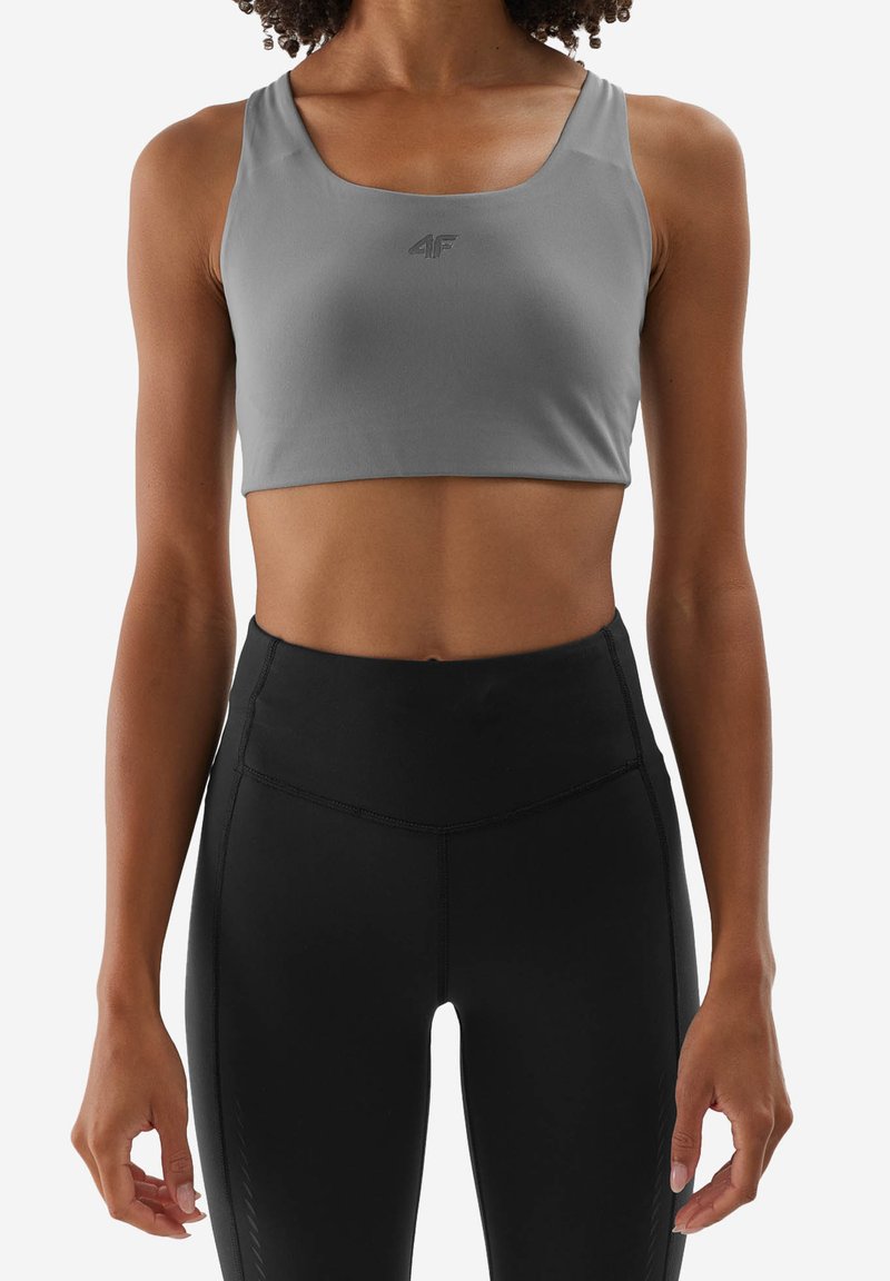 Šedá sportovní podprsenka s croptop designem, vyrobená z hladkého materiálu. Obsahuje malé logo na přední straně a široké ramínka.
