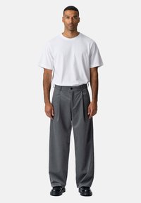 Hvid kortærmet t-shirt parret med løse, plisserede grå bukser og sorte sko. Stoffet er blødt; bukserne har et subtilt mønster.