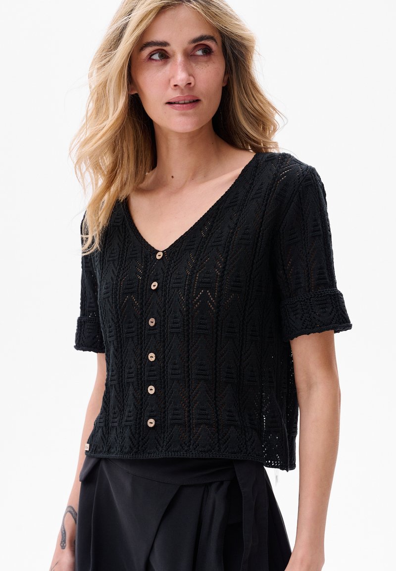 Czarny dzianinowy top z krótkim rękawem, z teksturowanym wzorem geometrycznym, dekoltem w kształcie litery V oraz drewnianymi guzikami z przodu. Skrócona długość.