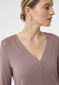 Helllila langärmliges Oberteil mit V-Ausschnitt und weichem Material. Der Strickstoff weist dezente Nähte auf und passt sich der Halslinie an.