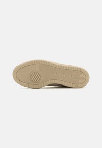 Beige sneakersåle med teksturert gummi, med et sirkulært mønster og merkevarelogo. Flat form med spor for grep.