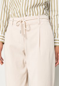 Beige lehké kalhoty s pasem na stažení, sklady a hladkým povrchem. Spárované se zeleno-bílým pruhovaným tričkem.