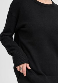 Pull noir en tricot texturé, avec un col large et des poignets côtelés, offrant une coupe décontractée et des poches latérales.