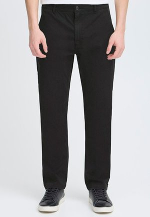 Black cotton trousers with a straight-leg cut, button closure, side pockets, and a smooth texture. Worn with black sneakers.