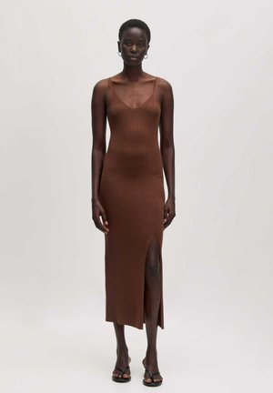 Brown ribbed knit dress with a V-neck, slim fit, and side slit, featuring thin straps and a mid-calf length, paired with black sandals.
