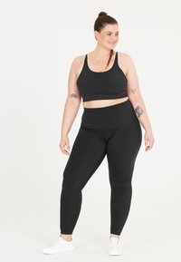 Zwart sportbeha en legging set gemaakt van rekbaar materiaal. De leggings hebben een gestructureerd ontwerp langs het onderbeen. Gecombineerd met witte sneakers.