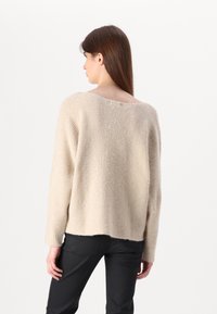 Bežinis megztinis, laisvo kirpimo, su plačiu apykakle ir ilgomis rankovėmis. Tekstūruota medžiaga su subtiliomis vertikaliomis juostelėmis. Siūlė yra šiek tiek trumpesnė.