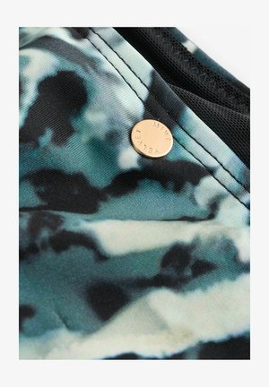 Zwart en teal patroonstof met een zachte textuur, voorzien van een metalen gouden ronde tag gemarkeerd met "MINI VET." Naaddetail zichtbaar.