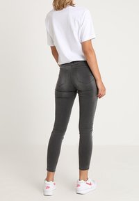 Jeans ajustados grises con cintura de media altura, diseño de cinco bolsillos y detalles de costura, combinados con una camiseta blanca sencilla y zapatillas blancas.