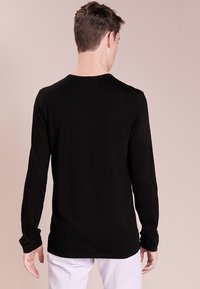 Maglietta nera a maniche lunghe realizzata in un tessuto leggero e morbido. Presenta un collo rotondo e un design semplice e senza decorazioni.