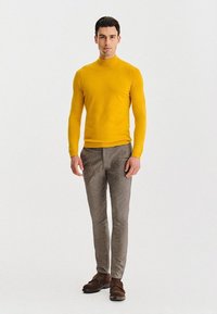Sweter z golfem w intensywnym żółtym kolorze, zestawiony z jasnoszarymi, dopasowanymi spodniami. Brązowe buty dopełniają stonowaną stylizację. Prosty, czysty design.