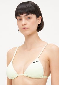 Svetlo žltý trojuholníkový bikiny vrch s tenkými nastaviteľnými ramienkami a čiernym logom Nike na ľavej strane. Hladká tkanina so zberaním detailingom.