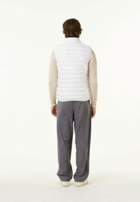 Witte puffer vest met een hoge kraag en horizontale stiksels. Draagt over een gestructureerde beige trui en gecombineerd met losse grijze broek.